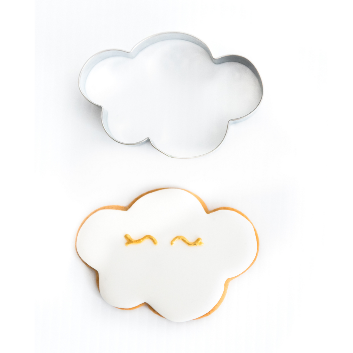 Coud cookie cutter and a gingerbread cloud cookie decorated with white royal icing and gold eyes